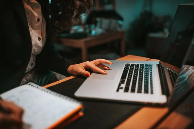 Mãos digitando em um notebook ao lado de um caderno de anotações